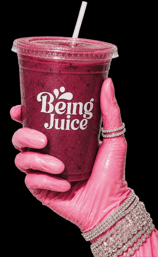 A hand holding a Being Juice berry smoothie